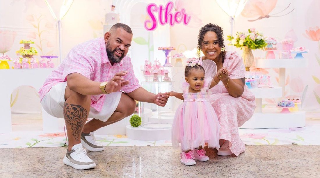 Pais agachados ao lado da filha, todos vestidos no tema rosa da festa